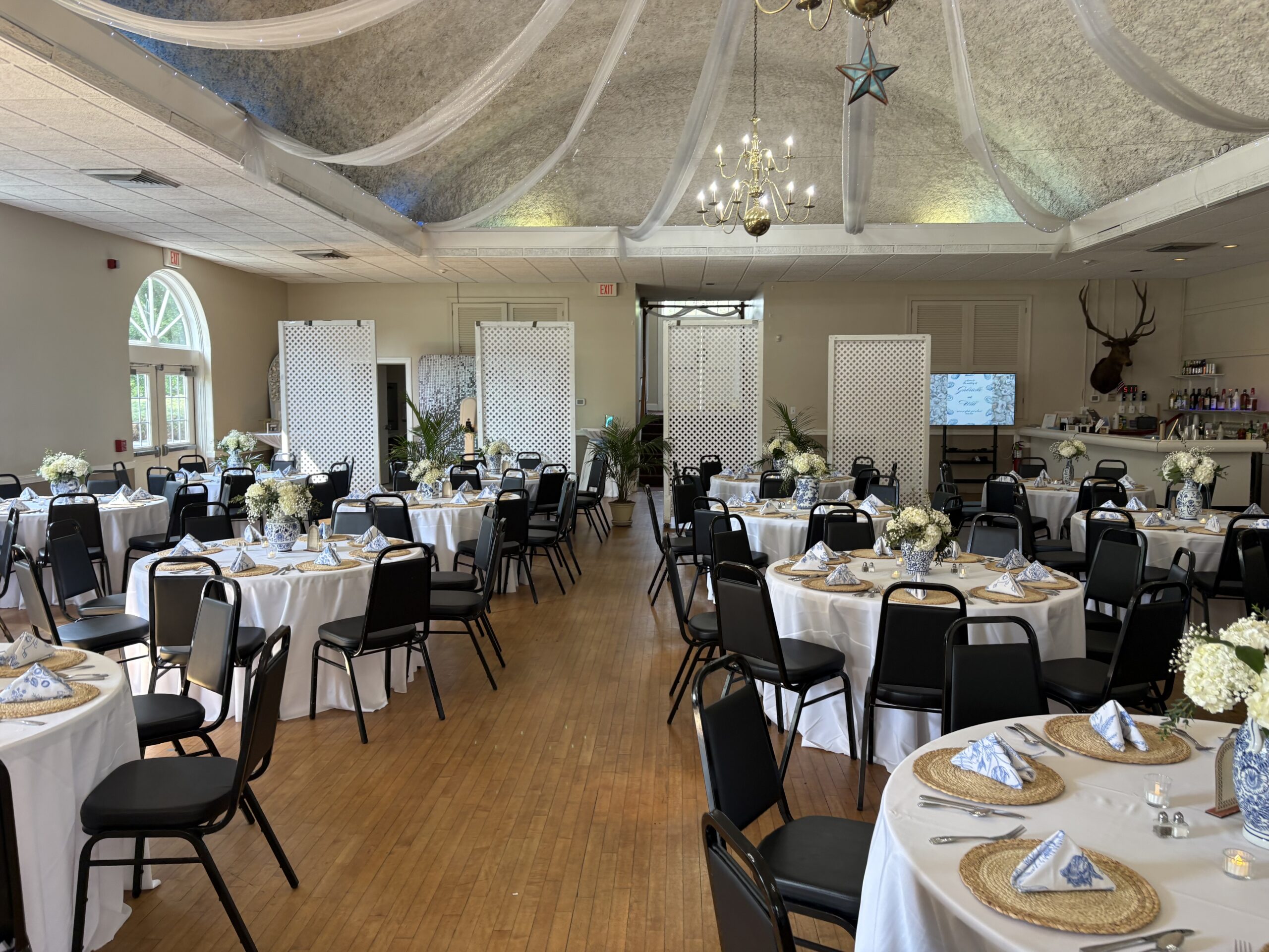 Round banquet tables with flowers beneath draped fabric and chandeliers.