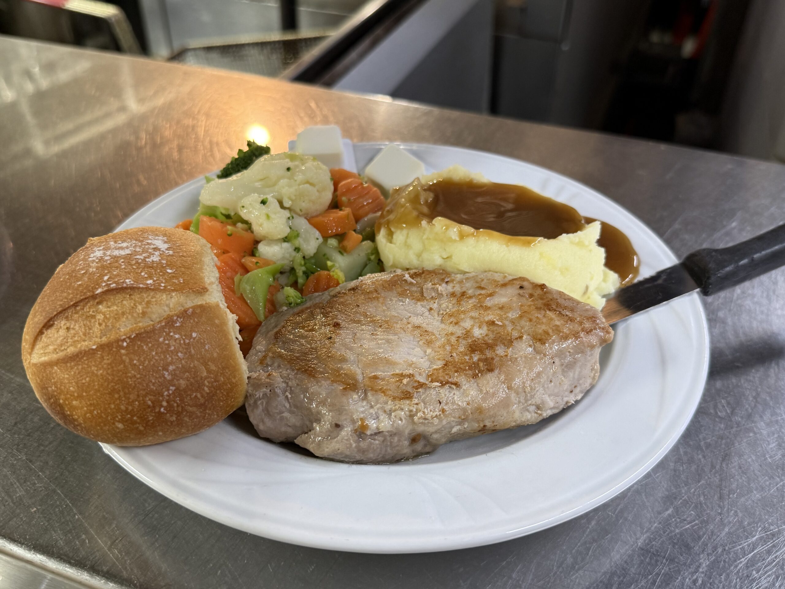 A plated Rathskeller dinner with mashed potatoes, gravy, vegetables and a roll.
